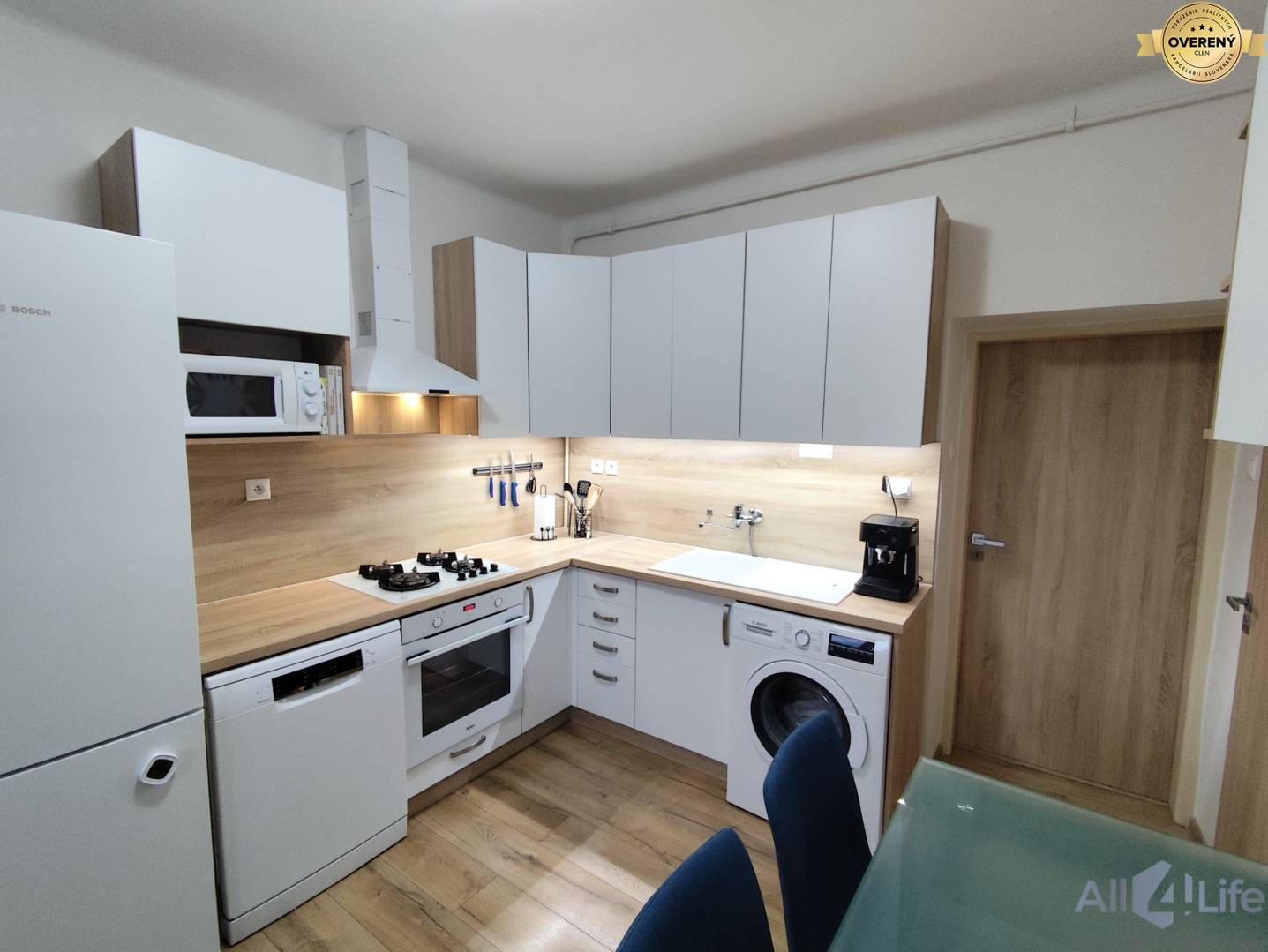 Kuchyňa s bielymi spotrebičmi a nábytkom, podlaha s dreveným dekorom v rodinnom dome.