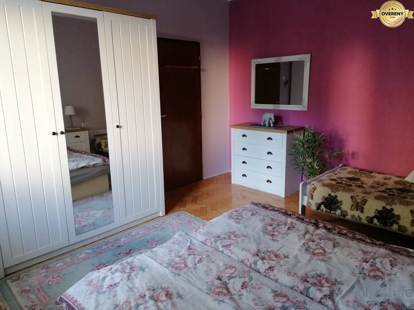 Spálňa v rodinnom dome s bielou skriňou a zrkadlom, ružové steny.