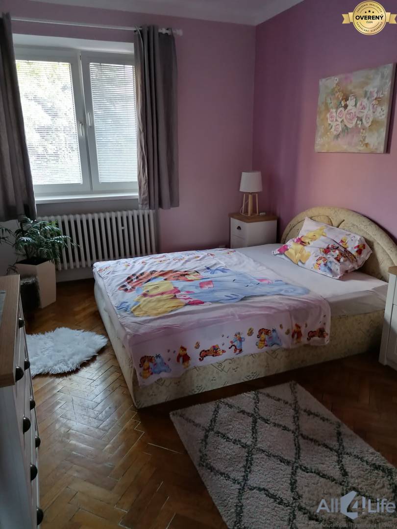 Ružová izba v rodinnom dome s posteľou, kobercami a podlahou s dreveným dekorom.