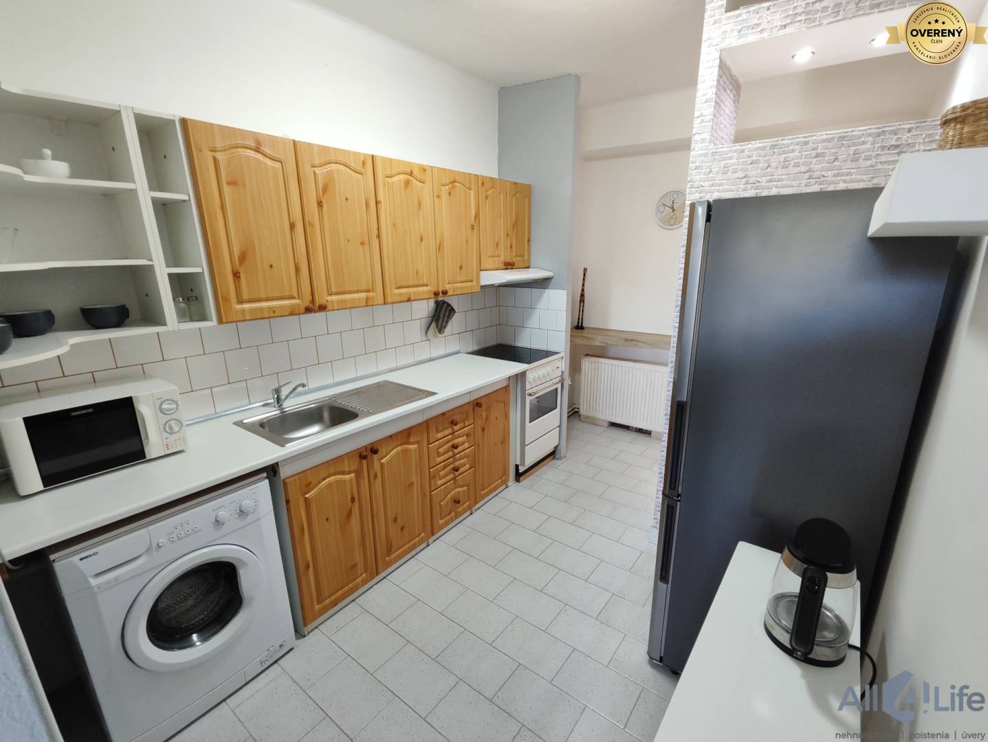 Kuchyňa v rodinnom dome s bielymi obkladačkami, drevenými skrinkami a vybavením.