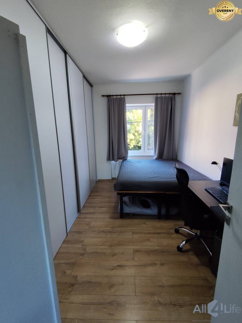 Spálňa v rodinnom dome s podlahou s dreveným dekorom, šatníkovou skriňou a pracovným stolom.