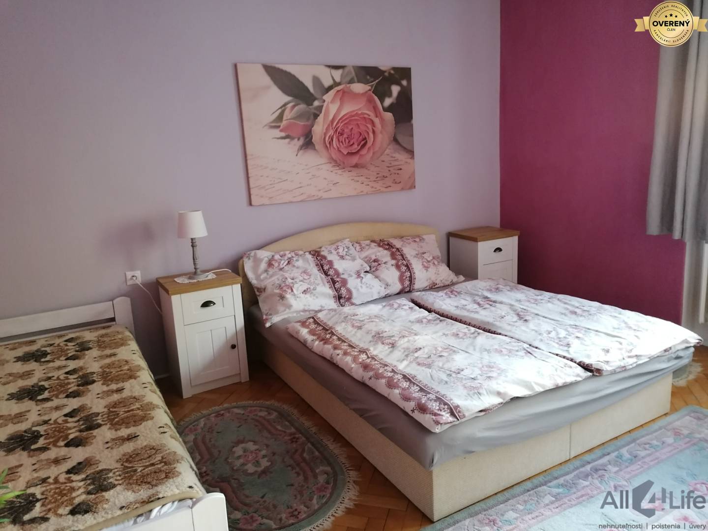 Spálňa v rodinnom dome s posteľou, fialovými stenami a podlahou s dreveným dekorom.