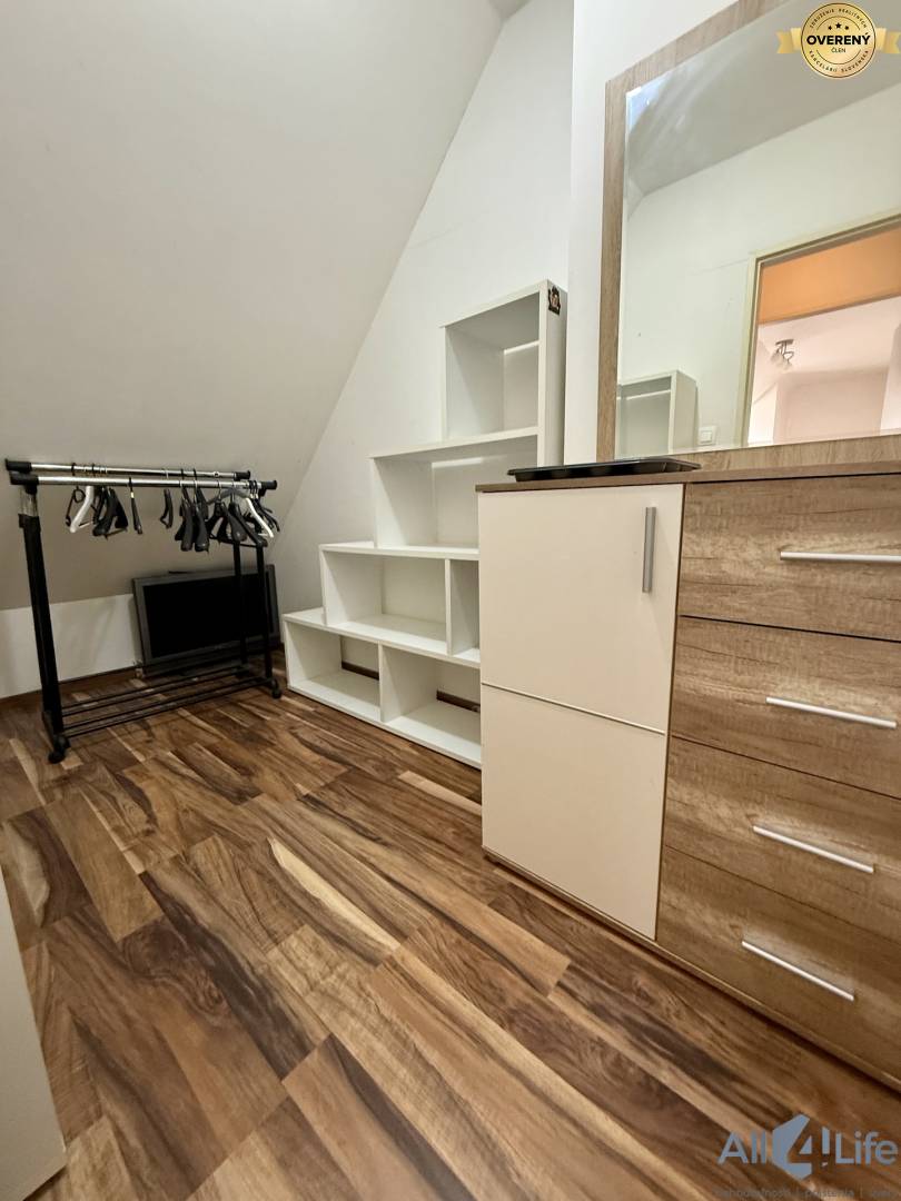 Interiér 2-izbového bytu s podlahou s dreveným dekorom, bielymi policami a zrkadlom.