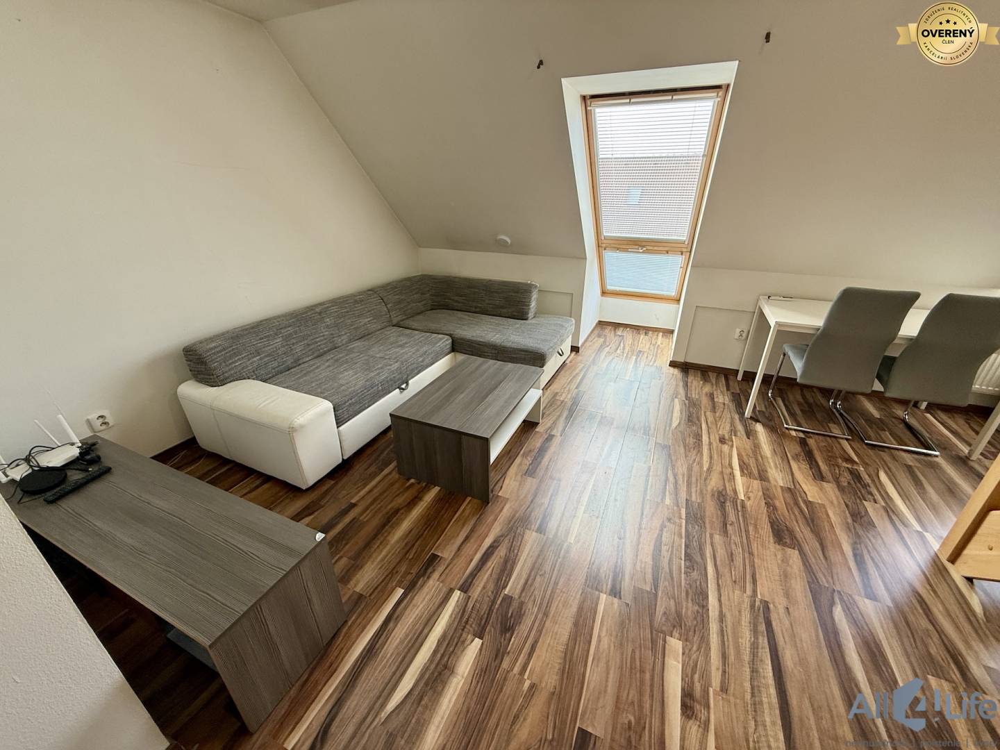 Podlaha s dreveným dekorom, sedačka, stôl a stoličky v 2-izbovom byte.