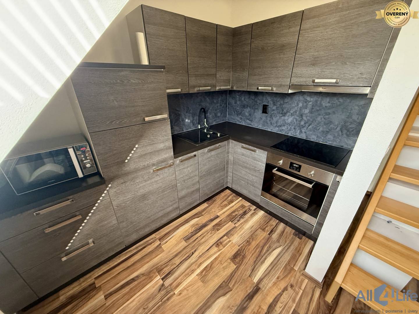 Kuchyňa v 2-izbovom byte s tmavými skrinkami a podlahou s dreveným dekorom.