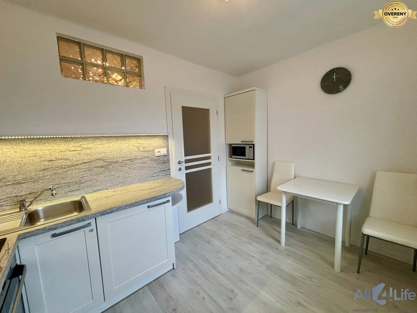 Kuchynský kút v 1-izbovom byte s podlahou s dreveným dekorom a jedálenským stolom.