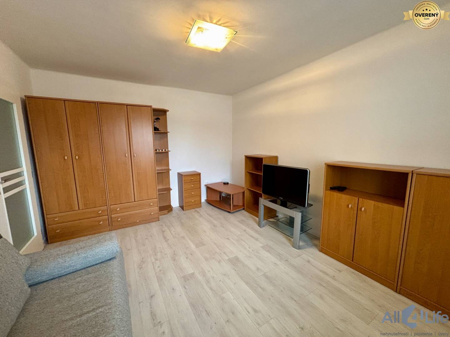 Obývacia izba v 1-izbovom byte s podlahou s dreveným dekorom a nábytkom.